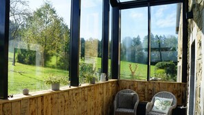 A wooden-paneled room with large windows overlooking a green landscape. There are two wicker chairs with cushions. - Charming house in the countryside (Havelange)