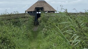 A thatched-roof structure with a narrow entrance, surrounded by tall grass and a wooden fence. - Luxury vacation home including boat and heated veranda in Stavoren (Stavoren)