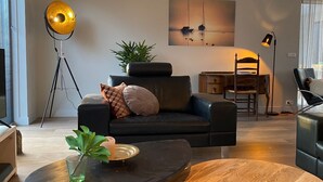A modern living room with a dark leather sofa, a round wooden coffee table, a floor lamp, and a painting of sailboats on the wall. - Luxury vacation home including boat and heated veranda in Stavoren (Stavoren)