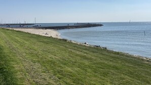 A coastal landscape with a grassy area, a sandy beach, and a rocky pier extending into the water. - Luxury vacation home including boat and heated veranda in Stavoren (Stavoren)