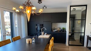 A modern kitchen with dark cabinetry, a large island, and a dining area with wooden chairs. - Luxury vacation home including boat and heated veranda in Stavoren (Stavoren)