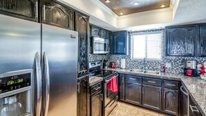 A modern kitchen with stainless steel appliances, dark cabinetry, and a tiled backsplash. - Private HEATED POOL at the Wine Time Villa! (Lake Havasu City)
