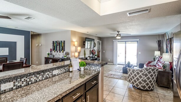 A spacious kitchen with granite countertops, a dining area with a table and chairs, and a living room with a sofa and a patterned ottoman. - Private HEATED POOL at the Wine Time Villa! (Lake Havasu City)