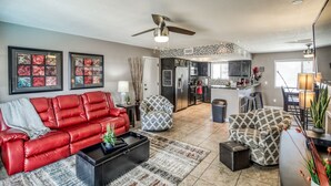 A modern living room with a red leather sofa, patterned armchairs, a black coffee table, and a kitchen in the background. - Private HEATED POOL at the Wine Time Villa! (Lake Havasu City)
