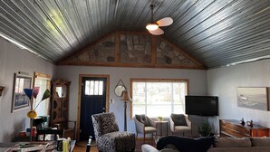 A cozy living room with a sloped ceiling, stone accents, a fireplace, and a television.