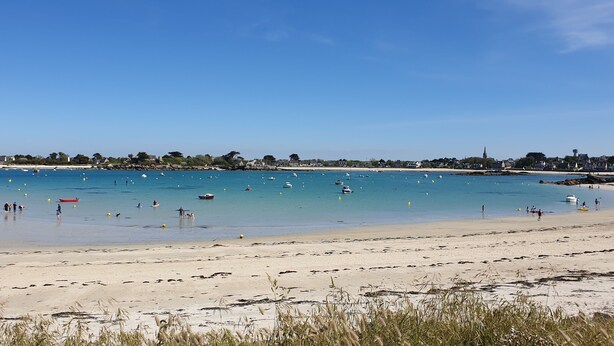 Une plage avec une eau d’un bleu limpide, des bateaux et des gens.