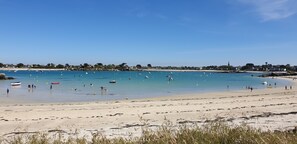 A beach with clear blue water, boats, and people.