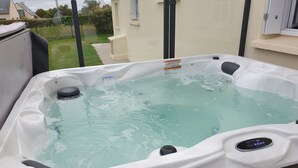 Un bain à remous doté d’un panneau de commande, entouré d’une terrasse en bois et offrant une vue sur un quartier résidentiel.