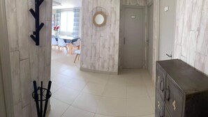Un couloir avec un mur en bois, un porte-manteau en métal, un coin repas avec une table et des chaises, et une porte.