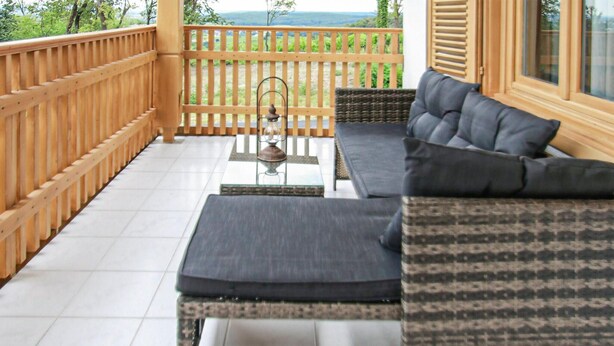 Un balcon doté d’une balustrade en bois, d’un canapé, d’une petite table et d’une lanterne.