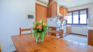 Una cocina con armarios de madera, una mesa de comedor con un jarrón de flores y una ventana con persianas.