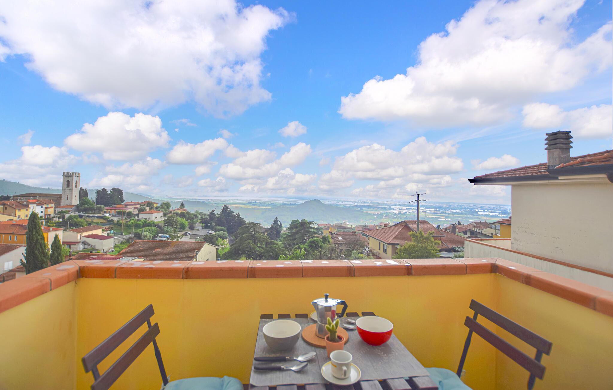 Ein Balkon mit Tisch für zwei Personen, mit Blick auf eine Stadt, einen Fluss und entfernte Berge.
