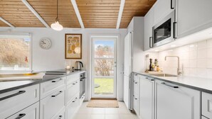 A modern kitchen with white cabinets, a wooden ceiling, and a view of the outdoors through a glass door.