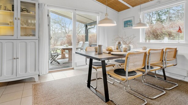 A dining area with a table and chairs, a cabinet with glass doors, and a view through a large window.