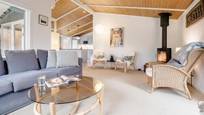 A living room with a sofa, wicker chairs, a glass coffee table, a fireplace, and a high ceiling with wooden beams.