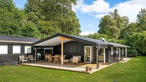 A modern, single-story cabin with a covered patio area, a barbecue grill, and a small deck.