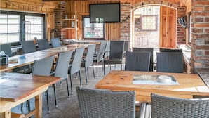 Een landelijke eethoek met houten tafels en rieten stoelen, bakstenen muren en een wandtelevisie.