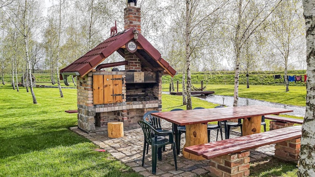 Een rustieke buitenkeuken met een bakstenen schoorsteen, houten kasten en een picknicktafel met bankjes.