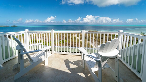 Un balcon doté de balustrades blanches et de deux fauteuils Adirondack donnant sur une mer bleue et dégagée et une île lointaine.