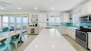Une cuisine moderne avec des meubles blancs, un îlot central et une vue sur l’extérieur.