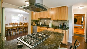 A kitchen with wooden cabinets, a granite countertop, a gas stove, and a dining area with chairs and a table. - Lovely spacious 6 BR home in St. Croix River valley (Taylors Falls)
