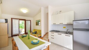 A compact kitchen with white cabinets, a stainless steel refrigerator, and a dining area with a table set for two. - 2 bedroom beautiful home in Bibione (Bibione)