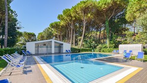 A swimming pool with blue tiles, surrounded by lounge chairs and a small building. - 2 bedroom beautiful home in Bibione (Bibione)