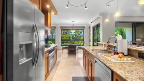 Une cuisine moderne dotée d’appareils électroménagers en acier inoxydable, d’un plan de travail en granit et offrant une vue sur un jardin luxuriant.