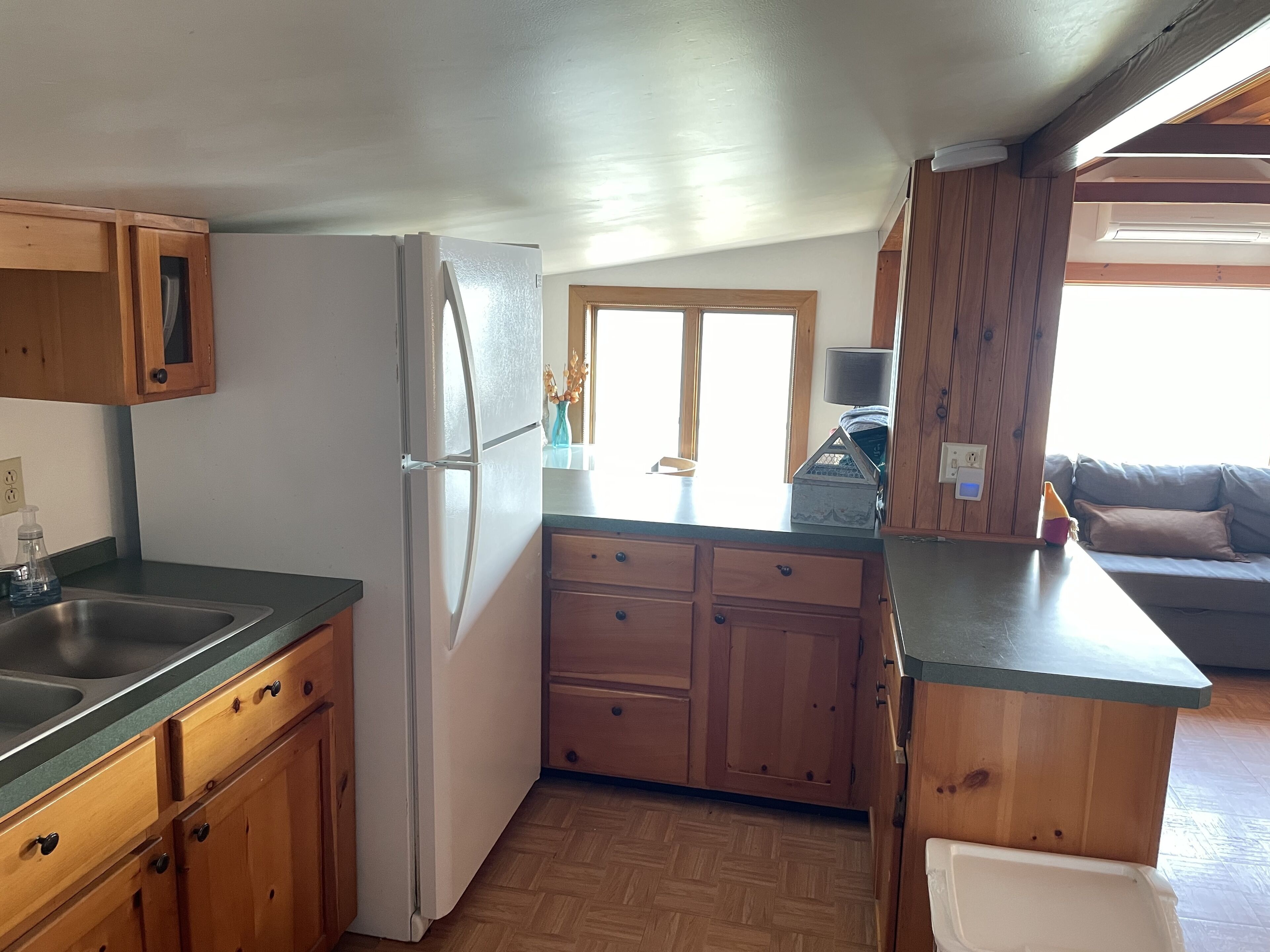 Une cuisine de taille réduite, dotée de meubles de rangement en bois, d’un réfrigérateur encastré et d’un plan de travail.