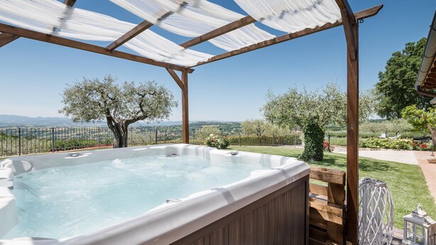 A hot tub under a wooden pergola with a view of a countryside landscape.