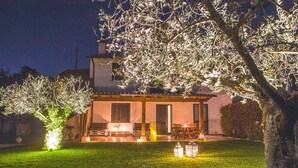 A two-story house with a patio, outdoor seating, and a well-lit garden at night.
