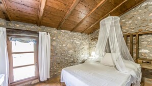 Une chambre avec un mur en pierre, un plafond en bois et un lit à baldaquin.