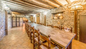 Une longue table en bois, des chaises, des murs en pierre et des poutres apparentes.