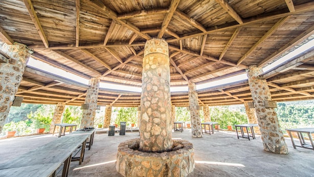 Un pavillon en plein air doté d’un plafond en bois et de piliers en pierre. Des tables et des chaises sont disposées pour permettre de prendre les repas à l’extérieur.
