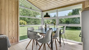 A dining area with a table and chairs, large windows, and a view of a garden.