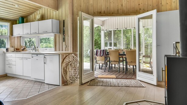 A modern kitchen with white cabinets, a built-in dishwasher, and a dining area with wicker chairs and a table.