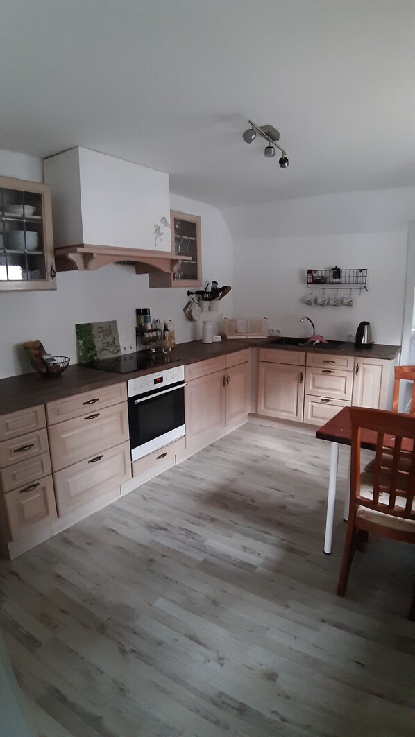 A kitchen with light wooden cabinets, a built-in oven, and a dining area with a wooden chair.