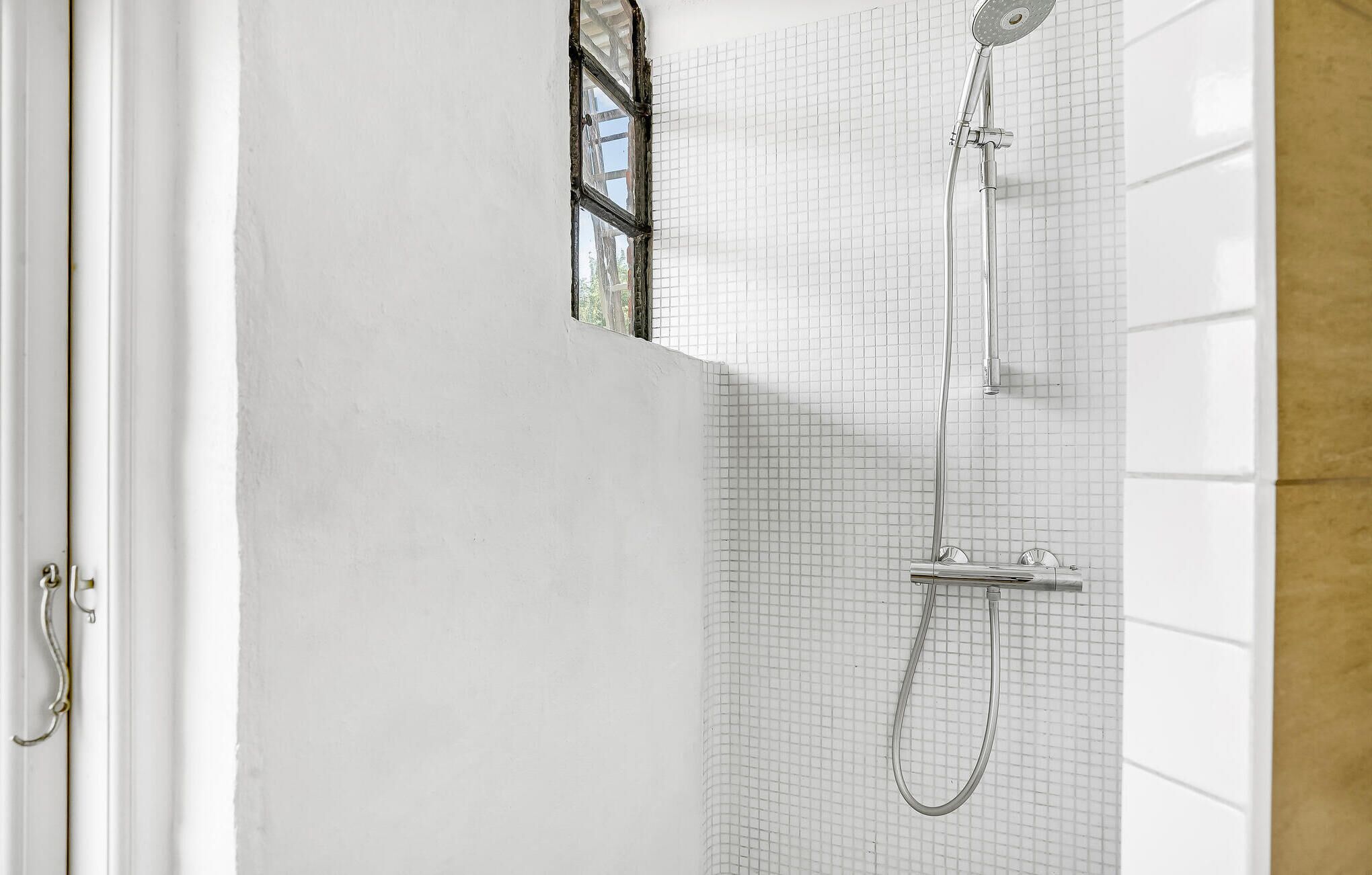 A bathroom with a shower, tiled walls, and a partially open door.