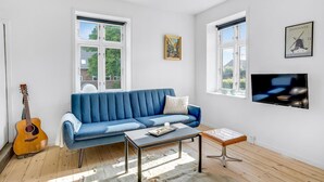 Un soggiorno con un divano blu, un tavolino da caffè, una chitarra e una TV appesa al muro.