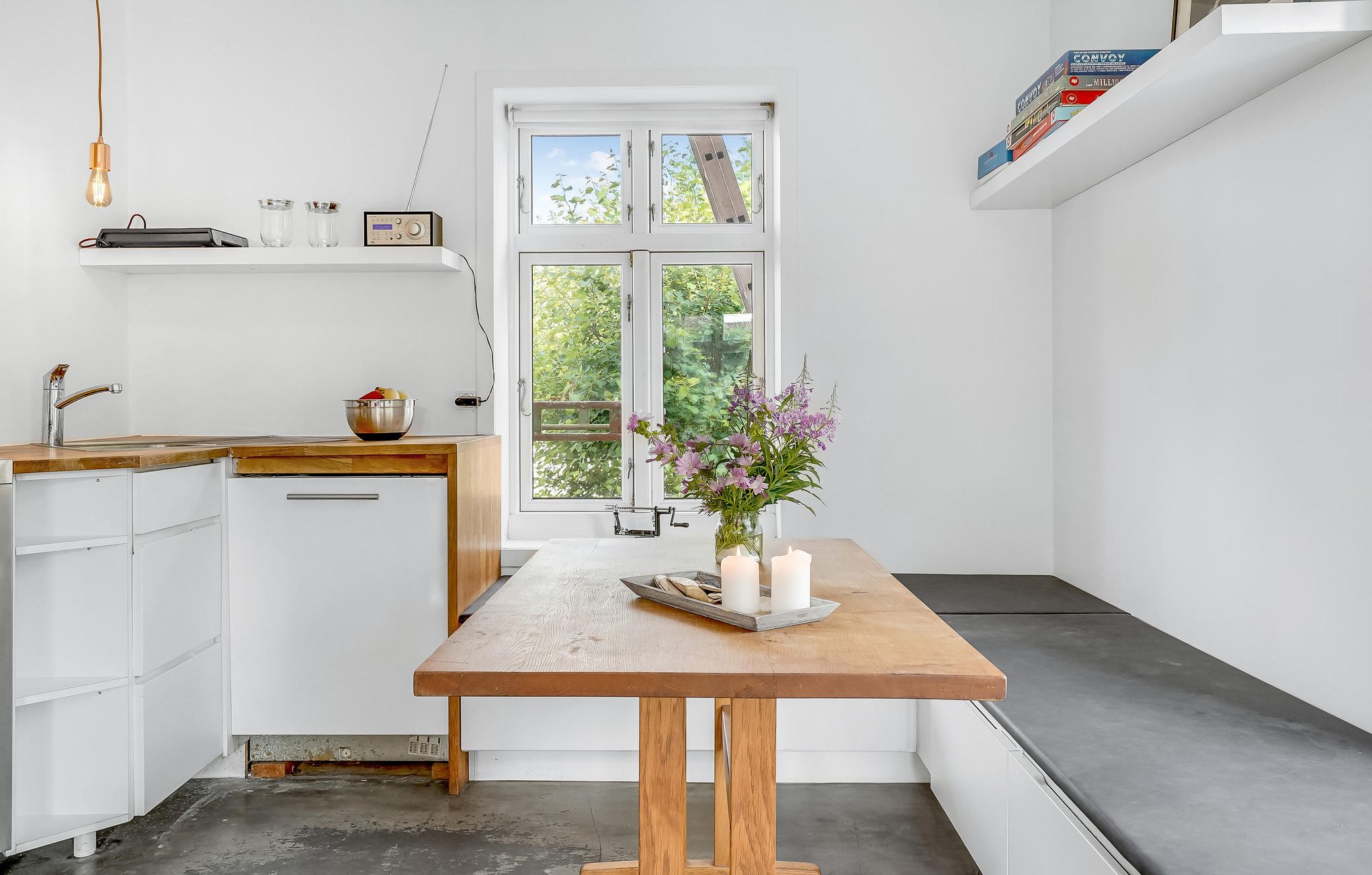 Une cuisine de taille réduite, avec une table en bois, des placards blancs et une fenêtre donnant sur un paysage verdoyant.