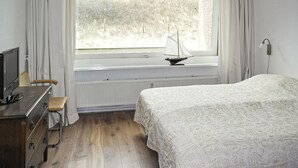 A bedroom with a bed, a small desk with a computer, a radiator, and a window with a sailboat model. - Cozy apartment in Bergen aan Zee (Bergen aan Zee)