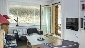 A modern living room with a leather sofa, a grey armchair, a wooden coffee table, and a TV mounted on the wall. - Cozy apartment in Bergen aan Zee (Bergen aan Zee)