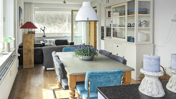 A modern kitchen with a dining area, featuring a large window, wooden flooring, and a white cabinet with glass doors. - Cozy apartment in Bergen aan Zee (Bergen aan Zee)