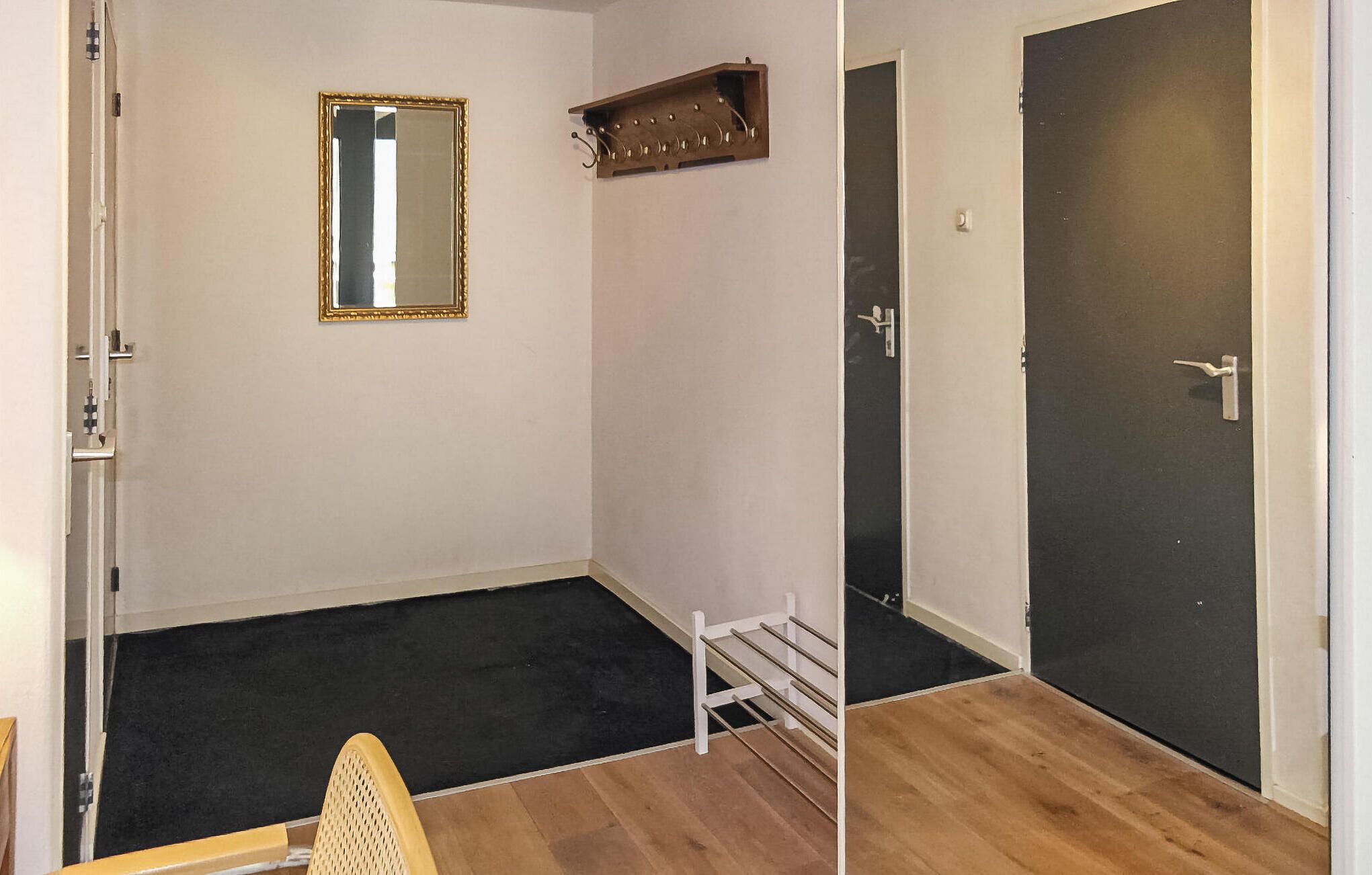 A room with a wooden floor, a white chair, a coat rack, a mirror, and a dark door.