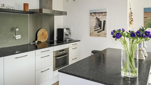 A modern kitchen with white cabinets, a black countertop, a coffee machine, and a vase with flowers. - Cozy apartment in Bergen aan Zee (Bergen aan Zee)