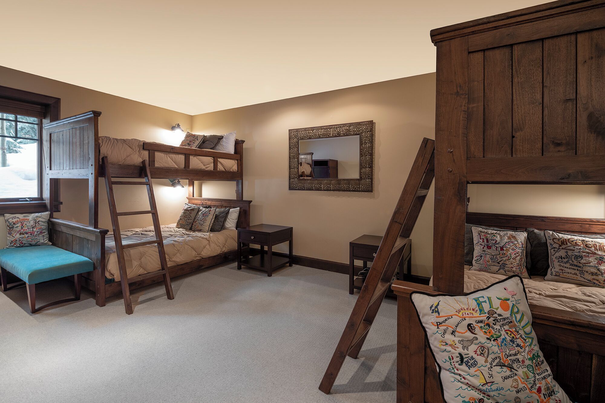 A cozy room with bunk beds, a ladder, a small desk, and a mirror.