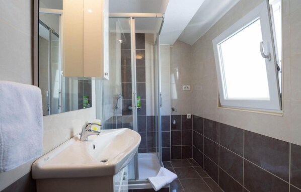 Une salle de bain avec une douche à parois de verre, un lavabo avec un miroir et une fenêtre laissant entrer la lumière naturelle.