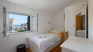 A small, bright room with a bed, a window with an open shutter, a wooden floor, and a white desk. - 4 bedroom beach front home in Split (Split)