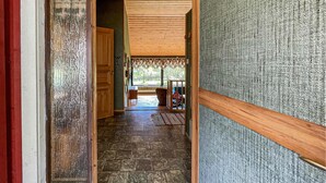 A hallway with a wooden door, a stone floor, and a view of a room with a window and a chair.