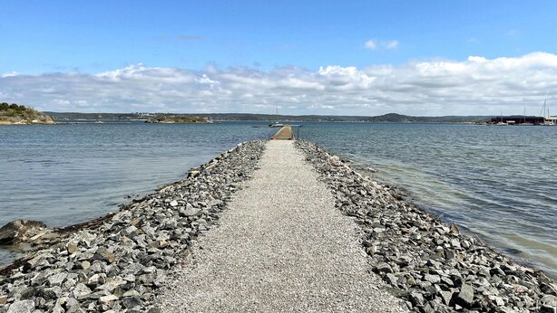 A rocky pier extending into calm water with a clear sky above.